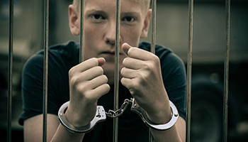 Handcuffed person holding prison bars.